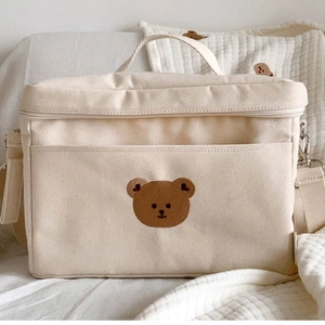 Detailed macro view of cream canvas diaper bag with brown bear embroidery and zipper