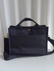 Detail of black canvas tote bag showing metal button closure and detachable shoulder strap