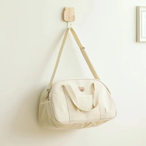Detail of embroidered bear on cream canvas diaper bag hanging on a wooden hook
