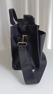 Detail view of the black tote bag featuring a functional side pocket and gold metal clips