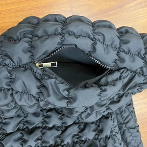 Detailed macro view of black quilted puffer bag featuring a gold zipper and fabric lining