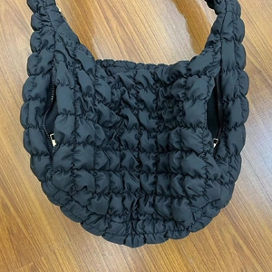 Close-up of black quilted hobo bag with cloud texture and gold zipper on wood floor