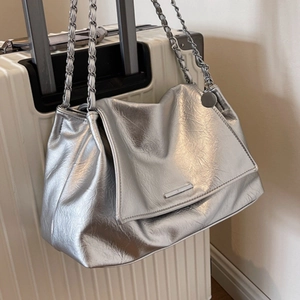 Metallic silver tote bag with crinkled texture and chain strap on a suitcase