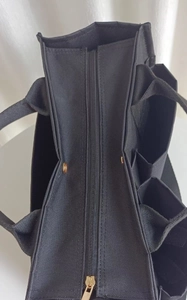 Close-up of black canvas tote bag showing multiple side pockets and gold zipper detail