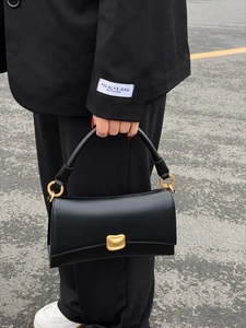 Foto street style di una borsa baguette in pelle nera con chiusura in oro opaco