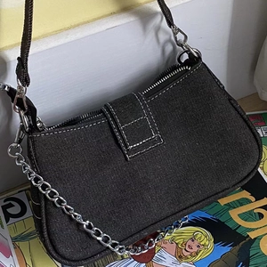 Detail of dark denim underarm bag with white stitching and metallic chain detail