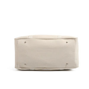 Close-up of beige canvas bag bottom featuring four silver metal protective feet and stitching