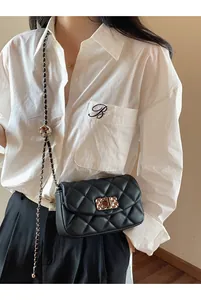 Detail of black quilted crossbody bag with golden hardware and metal chain strap