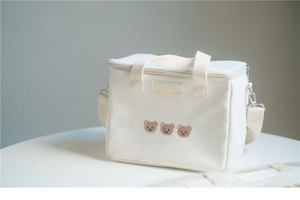 Detailed embroidery of three small brown bears on a cream-white canvas diaper bag