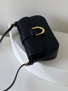 Sac bandoulière en cuir noir avec boucle dorée en fer à cheval, vue sous un angle de 45°