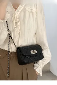 Detail of black quilted leather crossbody bag with adjustable silver ball chain on a model