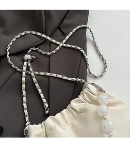 Detail einer cremefarbenen Kordeltasche mit geflochtenem Leder-Kettenriemen und Marmorperle