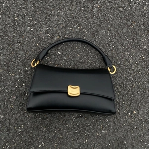 Borsa baguette minimalista in pelle nera con fibbia dorata ondulata su pietra