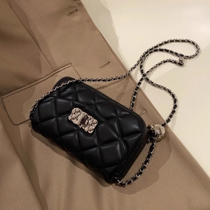 Quilted black leather flap bag with silver chain and metal ball adjustment on a trench coat