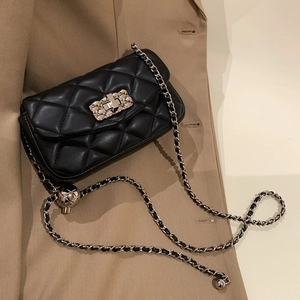 Classic black quilted crossbody bag with golden ball chain on elegant camel coat