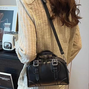 Chic black Boston bag with silver buckle details worn as a crossbody in a cozy lifestyle setting