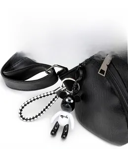 Detail of a bear figurine charm with a woven lanyard on a black textured leather backpack