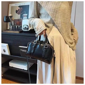 Detail shot of black Boston handbag with glossy leather finish and metal buckle closure