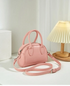 Close-up of a pale pink mini Boston bag with adjustable strap on a white desktop