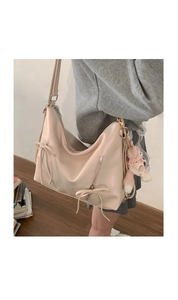 Detail of cream white hobo bag with bow decoration and plush charm on a wide shoulder strap