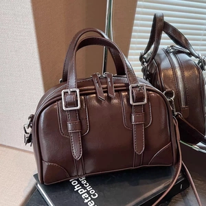 Caramel brown Boston bag with glossy oil-wax leather texture shown via mirror reflection