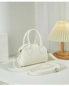Close-up of a white mini Boston bag with silver zippers and adjustable strap on a desk