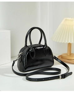 Detail view of a glossy black leather Boston bag with silver hardware and top handles