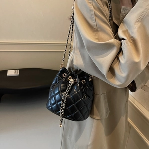 Detail of black quilted leather bucket bag with gold chain strap and drawstring closure