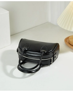 Detail of glossy black Boston bag featuring round handles and polished silver zipper