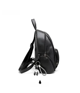 Side view of a black faux leather backpack with layered compartments and bear charm