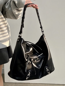 Close-up of black tote bag with silver studs, buckles, and long tassels detail