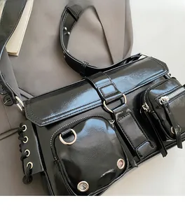 Close-up of black glossy faux leather crossbody bag with multiple zippers and metal hardware