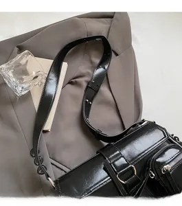 Detail view of glossy black leather baguette bag with silver buckles and adjustable strap