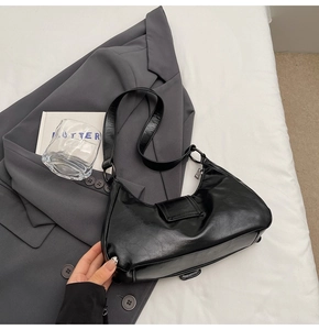 Detail of glossy black PU leather hobo bag on grey suit jacket with minimalist styling