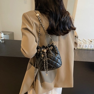 Woman wearing a black quilted bucket bag with gold chain strap over a camel blazer