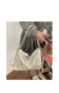 Detailed view of cream-white tote bag featuring bow accents and vertical zippers