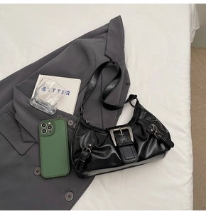 Detail view of black pleated underarm bag with large metal buckle on soft suit background