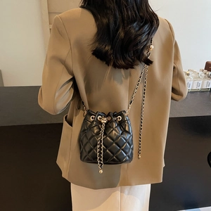 Close-up of black quilted bucket bag with golden chain drawstring and leather woven strap