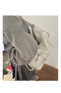 Detail view of cream PU leather backpack with bow ribbons worn by a model in casual style