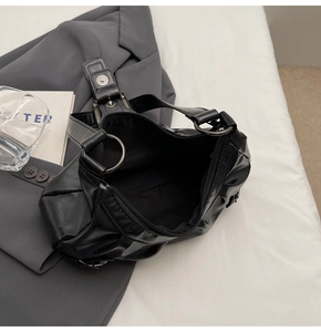 Detail of black PU leather shoulder bag interior and metallic hardware on grey suit backdrop