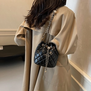 Detailed back view of a black quilted bucket bag with gold chain strap on a model