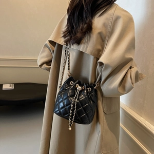 Detail of a black quilted bucket bag featuring a chain strap and gold sphere drawstring