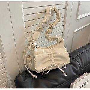 Detail of cream white pleated shoulder bag with scrunchie handle and bow on leather bench