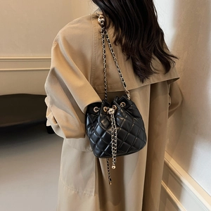Detail of black quilted leather drawstring bucket bag with gold chain and pendant