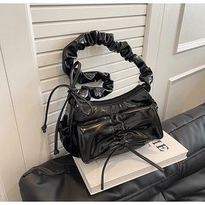 Detail of black glossy pleated cloud bag featuring a decorative bow and zipper closure