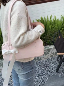 Detail of pink baguette bag with white ribbon bow decoration worn as a shoulder bag