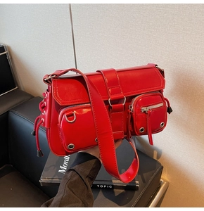 Detail view of red glossy underarm bag featuring utility pockets and metallic hardware