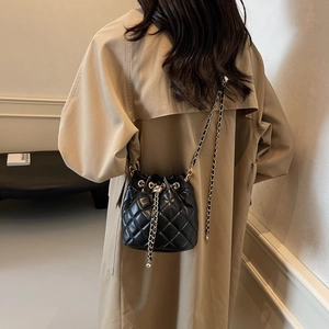 Quilted black bucket bag with gold chain strap worn with a stylish trench coat