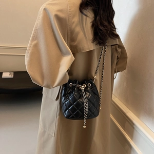 Detail view of quilted black bucket bag with chain strap on a model wearing trench coat