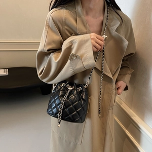 Detail of black quilted mini bucket bag with gold chain strap on a khaki coat